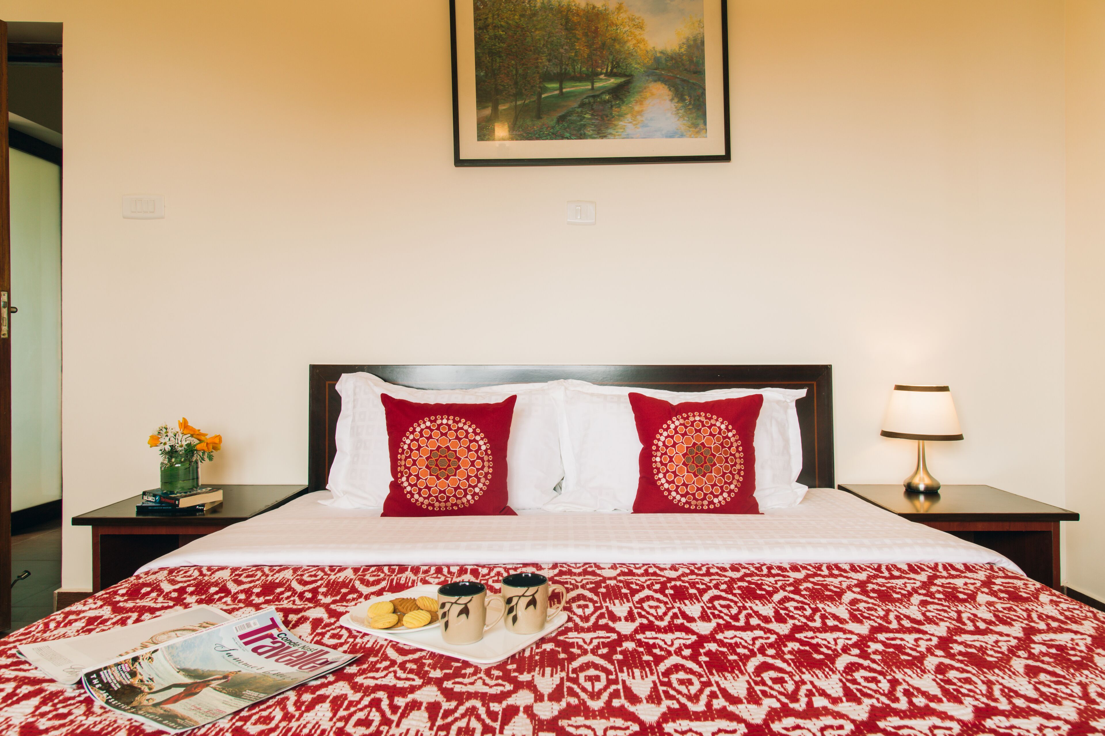 Un lit bien fait, recouvert d’une couvre-lit à motifs, avec deux coussins décoratifs, un plateau contenant des biscuits et des tasses, et un magazine posé sur le lit.