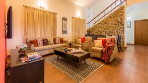 Una sala de estar con sofá, sillón y mesa de centro, una escalera con pared de piedra y una puerta de madera.