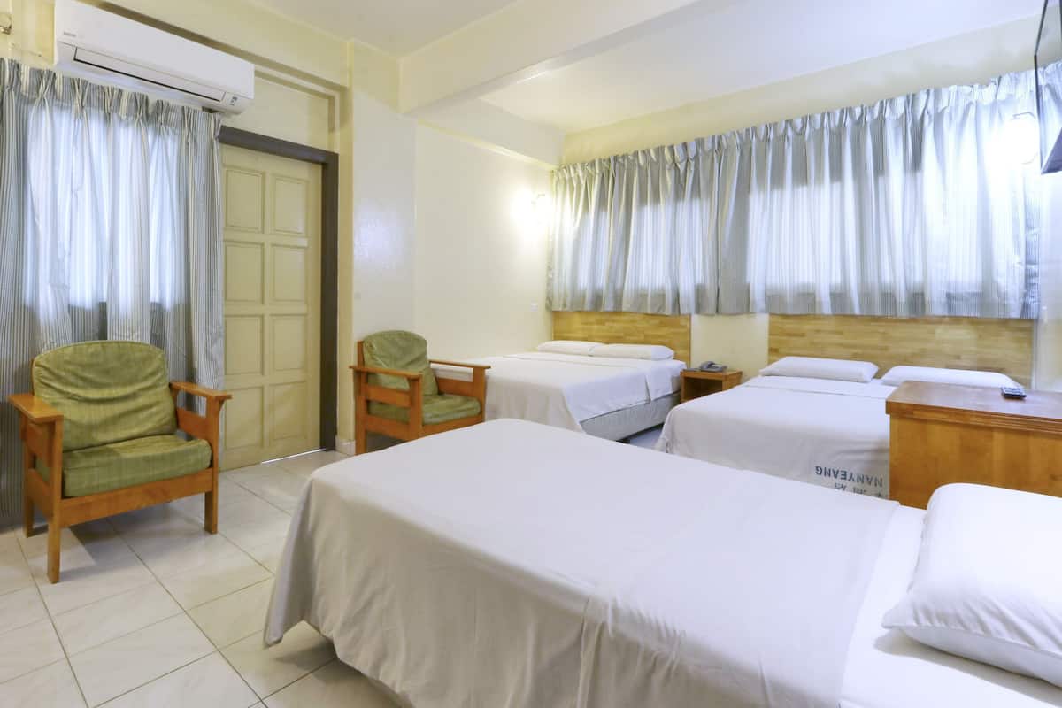 A hotel room with two single beds, a wooden nightstand, a green chair, and a window with curtains.