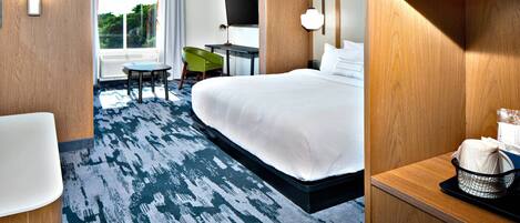 A hotel room with a large bed, a desk with a flat-screen TV, a green chair, and a small table.