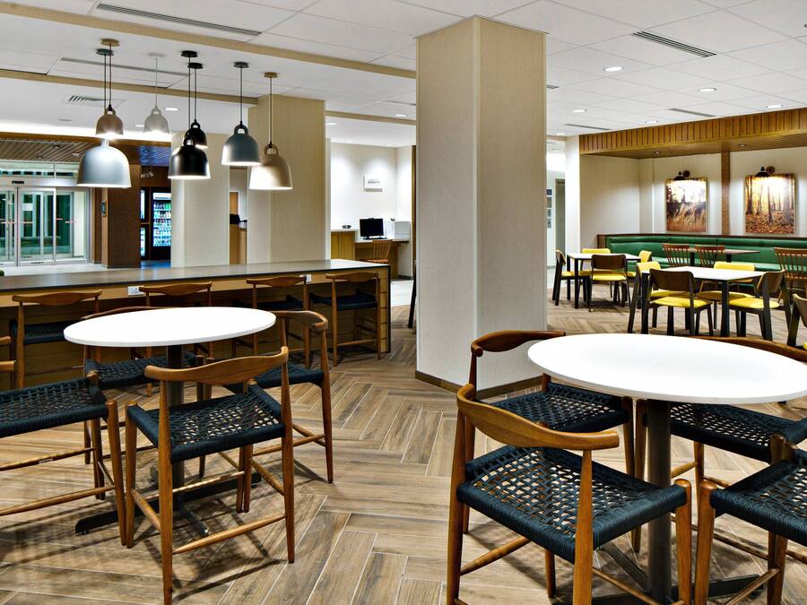 Een restaurant in een hotel, met ronde tafels, rieten stoelen en hanglampen.