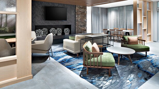 A modern living room with a fireplace, a flat-screen TV, and a dining area with a table and chairs. - Fairfield by Marriott Inn & Suites Deerfield Beach Boca Raton (Deerfield Beach)