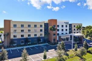 Un hotel de varios pisos con diseño moderno, que presenta una combinación de colores beige y azul en su fachada, una entrada central y un estacionamiento con espacios delimitados.