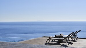 Een houten terras met lounge fauteuils en een tafel, met uitzicht op een rustige zee.