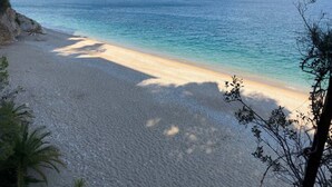 Een strand met helder water, een zandstrand en bergketens in de verte.