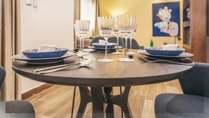 A dining table set with blue plates, clear glasses, and cutlery, with a painting on the wall and a lamp in the background. - Appartement Meublé VIP Douala Bonapriso (Douala)