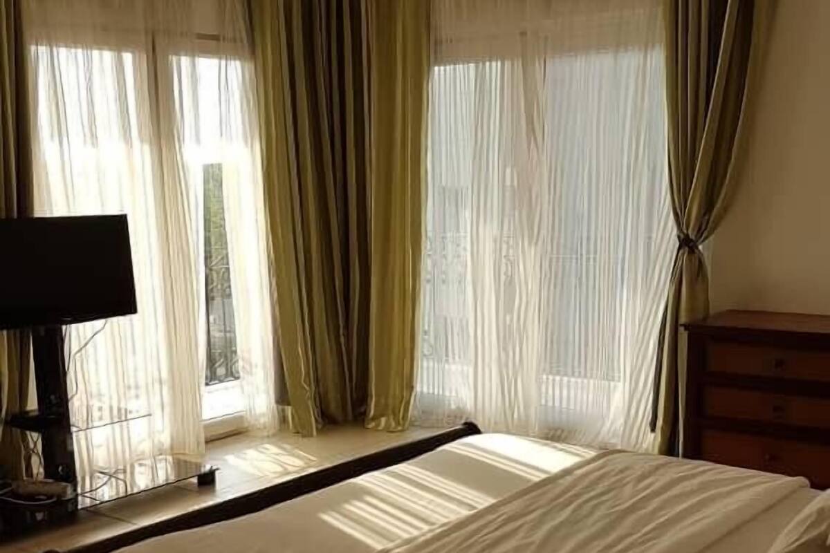 A bedroom with a bed, curtains, a television, and a wooden dresser.