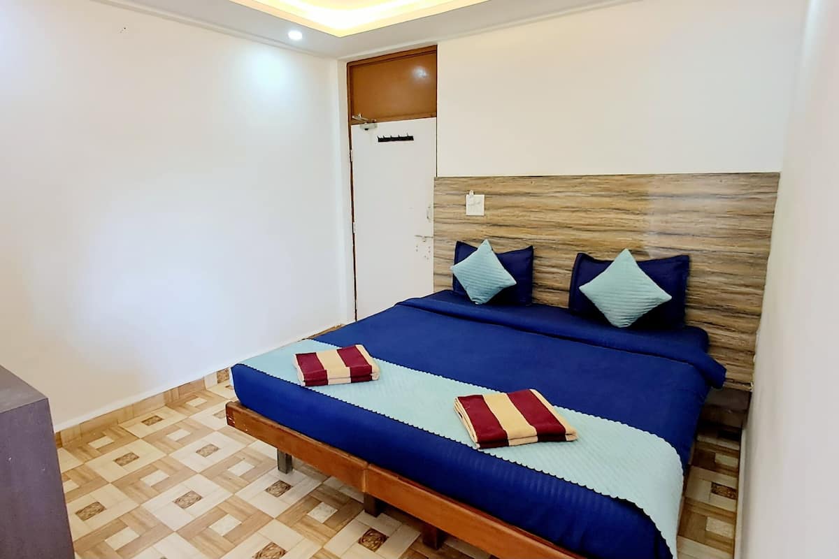 A bedroom with a wooden headboard, a bed with blue bedding and decorative pillows, a bedside table, and a small plant on a shelf.