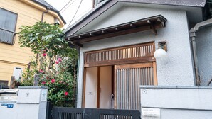 Ein traditionelles japanisches Haus mit einer Holztür, einem kleinen Garten mit rosa Blumen und einem schwarzen Tor.