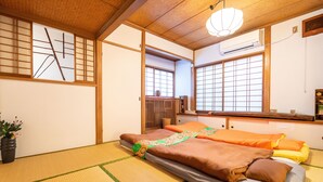 Ein traditioneller japanischer Raum mit Tatami-Böden, einem Futon-Bett, gleitenden Shoji-Schiebetüren und einem Blick ins Freie durch ein Fenster.