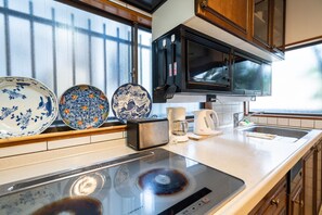 A kitchen with a built-in microwave, toaster, and electric kettle. There are decorative plates on the counter and a window with blinds. - Villa Traditional Designer House Oyama (Tokyo)