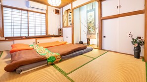 Ein traditioneller japanischer Raum mit Tatami-Bodenbelag, Futon-Bett, Schiebetüren und Blick durch einen Shoji-Bildschirm.