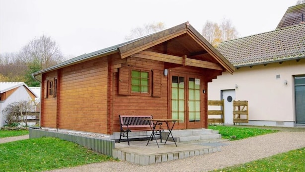 Una cabaña de madera con techo inclinado, una banca y una mesa en el exterior.