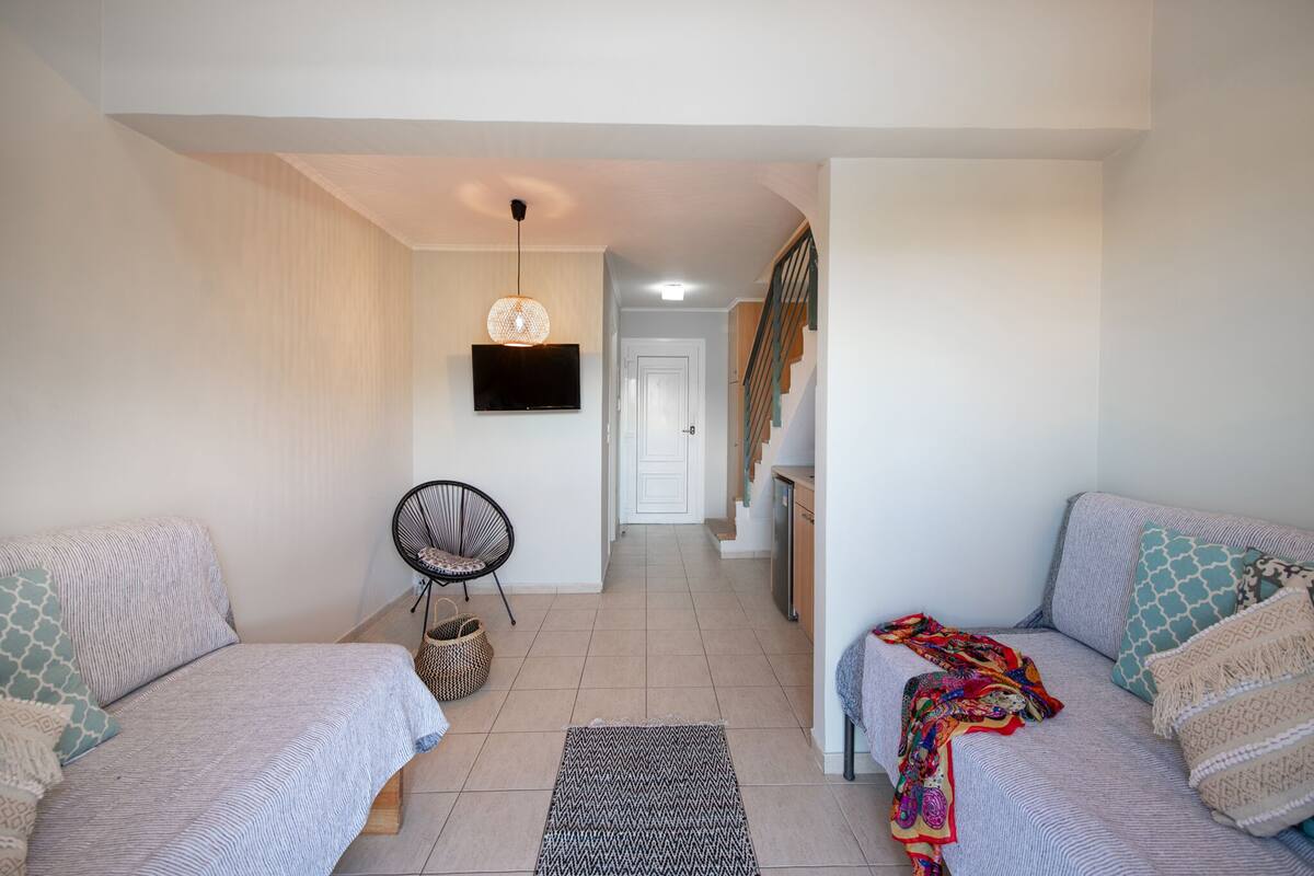 Una sala de estar moderna con dos sofás, un televisor, una silla y una escalera.
