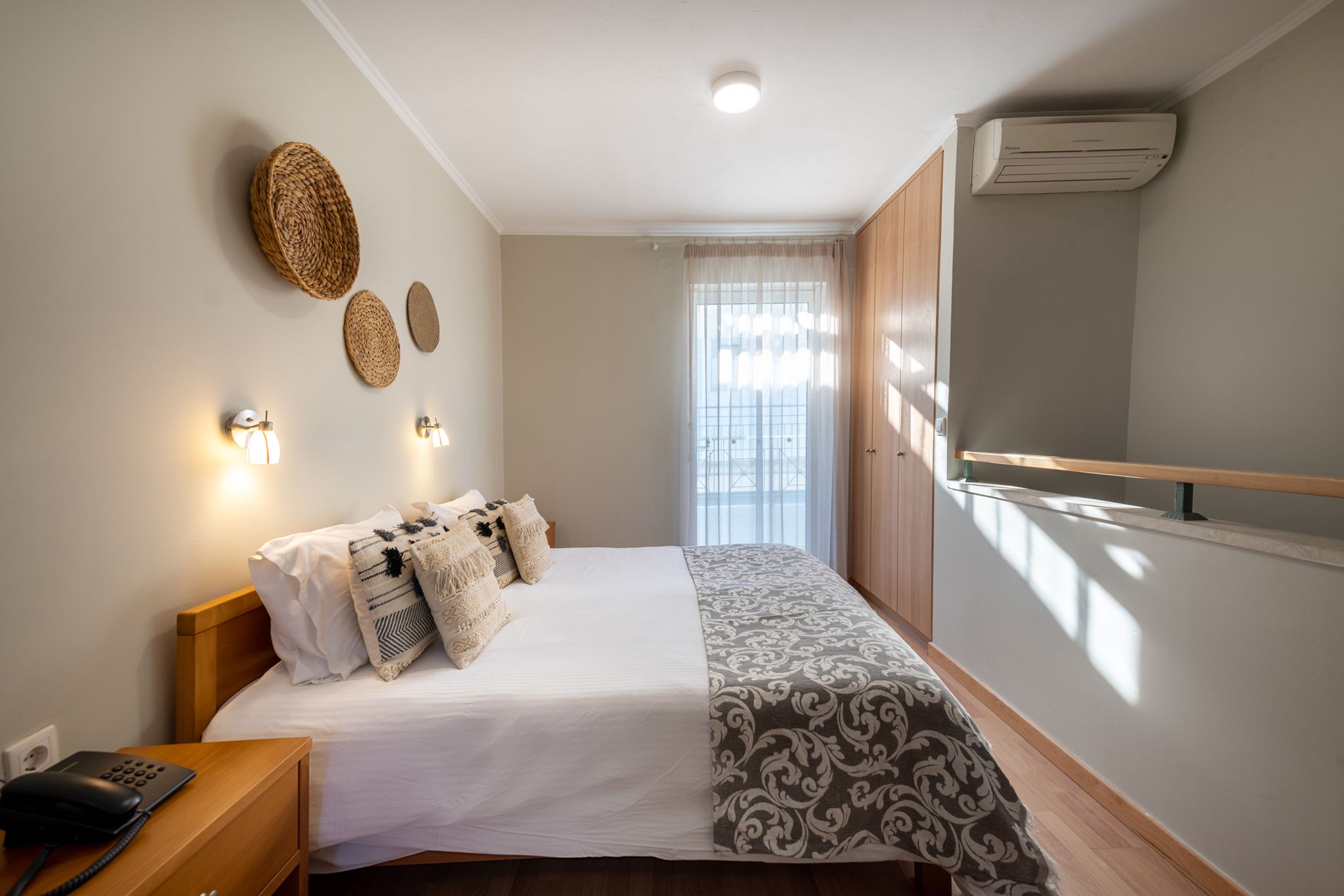 Habitación de hotel ordenada con cama, mesita de noche, lámpara y aire acondicionado de pared.
