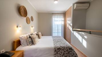 Habitación de hotel ordenada con cama, mesita de noche, lámpara y aire acondicionado de pared.