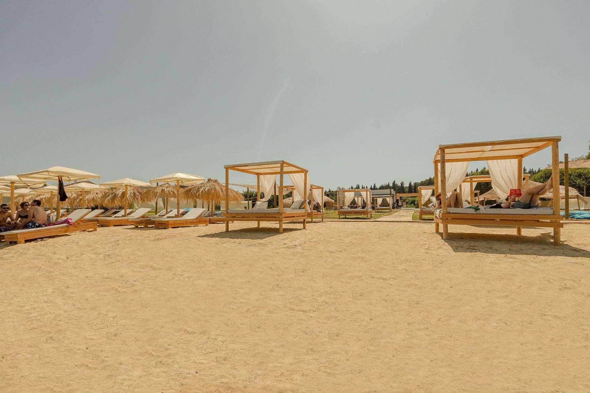 Una playa con camas y sombrillas de madera, cielos despejados y arena.