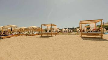 Una playa con camas y sombrillas de madera, cielos despejados y arena.