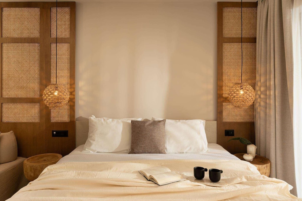 Una cama bien hecha con un libro y dos tazas, un cabecero de madera y dos paneles de pared tejidos con lámparas colgantes.