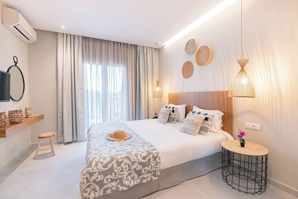 A modern hotel room with a large bed, a small round table, a wall-mounted TV, and a ceiling fan.