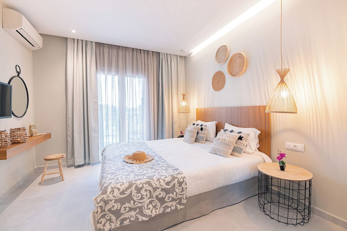 Una habitación de hotel moderna con una cama grande, una mesita redonda pequeña, un televisor montado en la pared y un ventilador de techo.