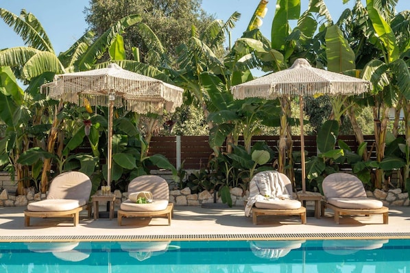A poolside area with lounge chairs and straw umbrellas, surrounded by banana trees.