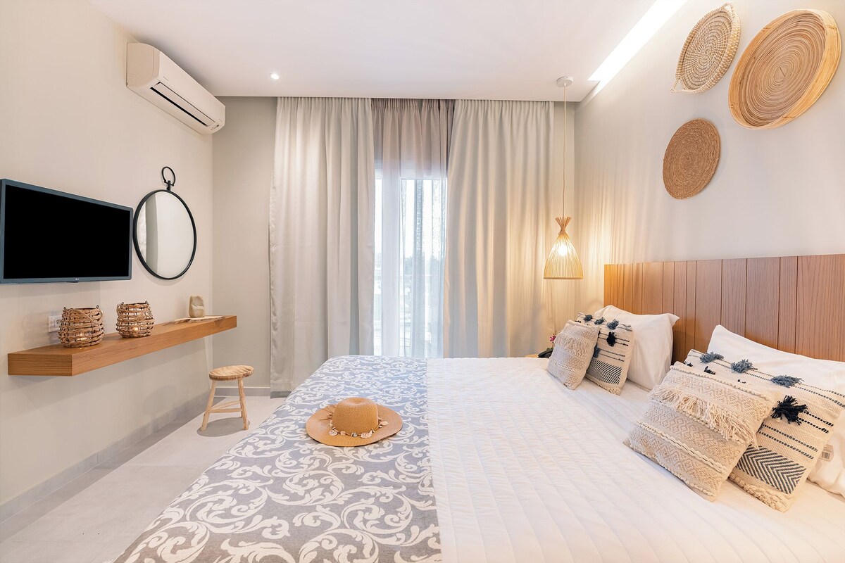 Ein modernes Hotelzimmer mit Bett, einem Wandfernseher, einer Ablage mit Dekoration, einem Fenster mit Vorhängen und einer Wandklimaanlage.
