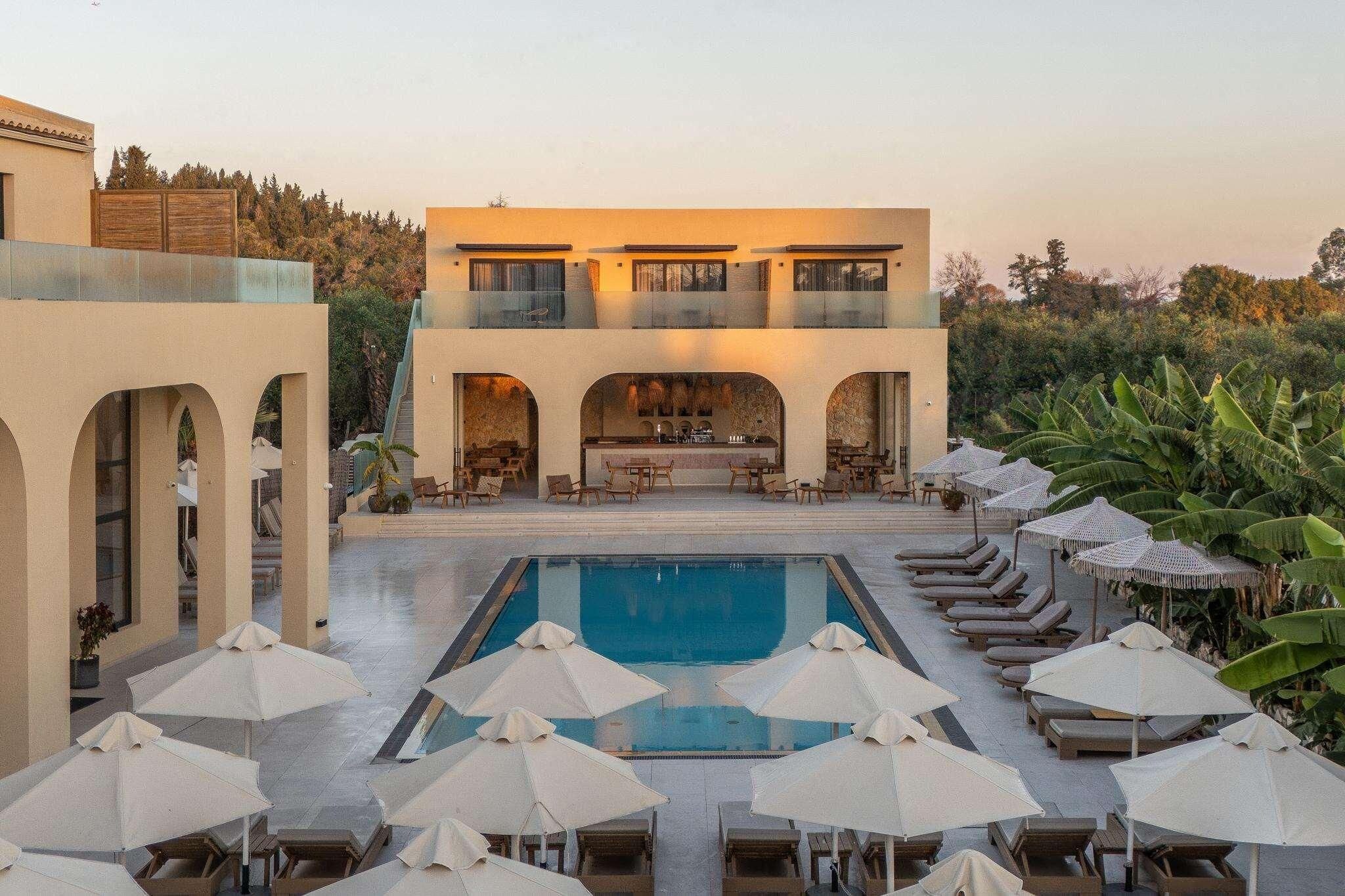 A poolside area with lounge chairs and umbrellas, a bar, and a two-story building with balconies.