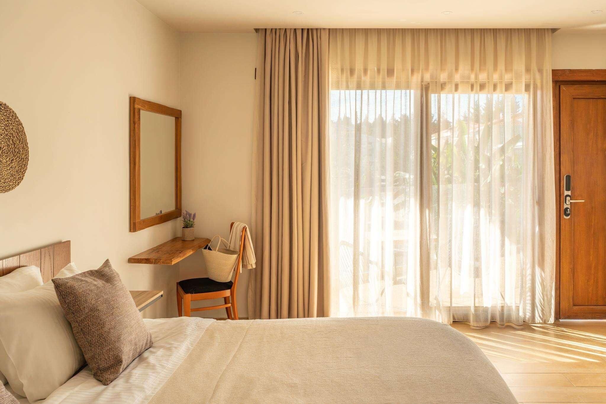 A bedroom with a bed, a chair, a desk, a mirror, and a door.