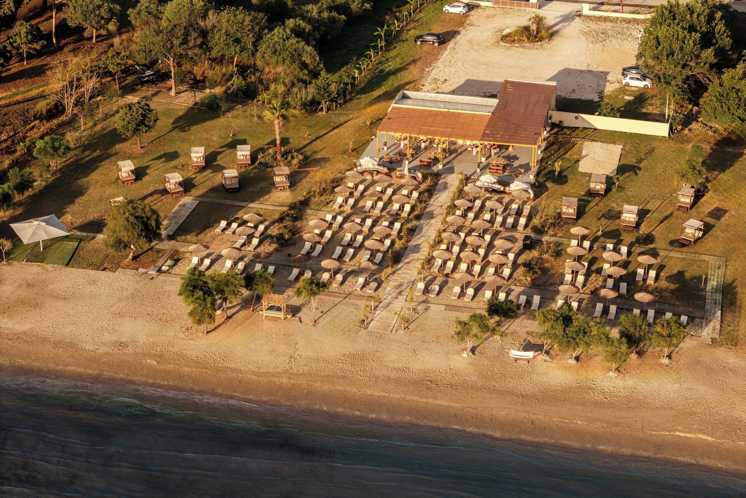 Eine Luftaufnahme eines Strandanwesens mit mehreren Bungalows, einem zentralen Gebäude mit rotem Dach und einem Sandstrand.