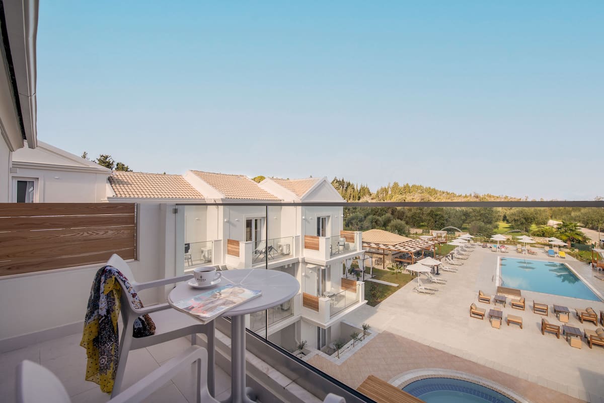 Un balcón con mesa, sillas y vistas a un área de piscina con sillones y sombrillas.