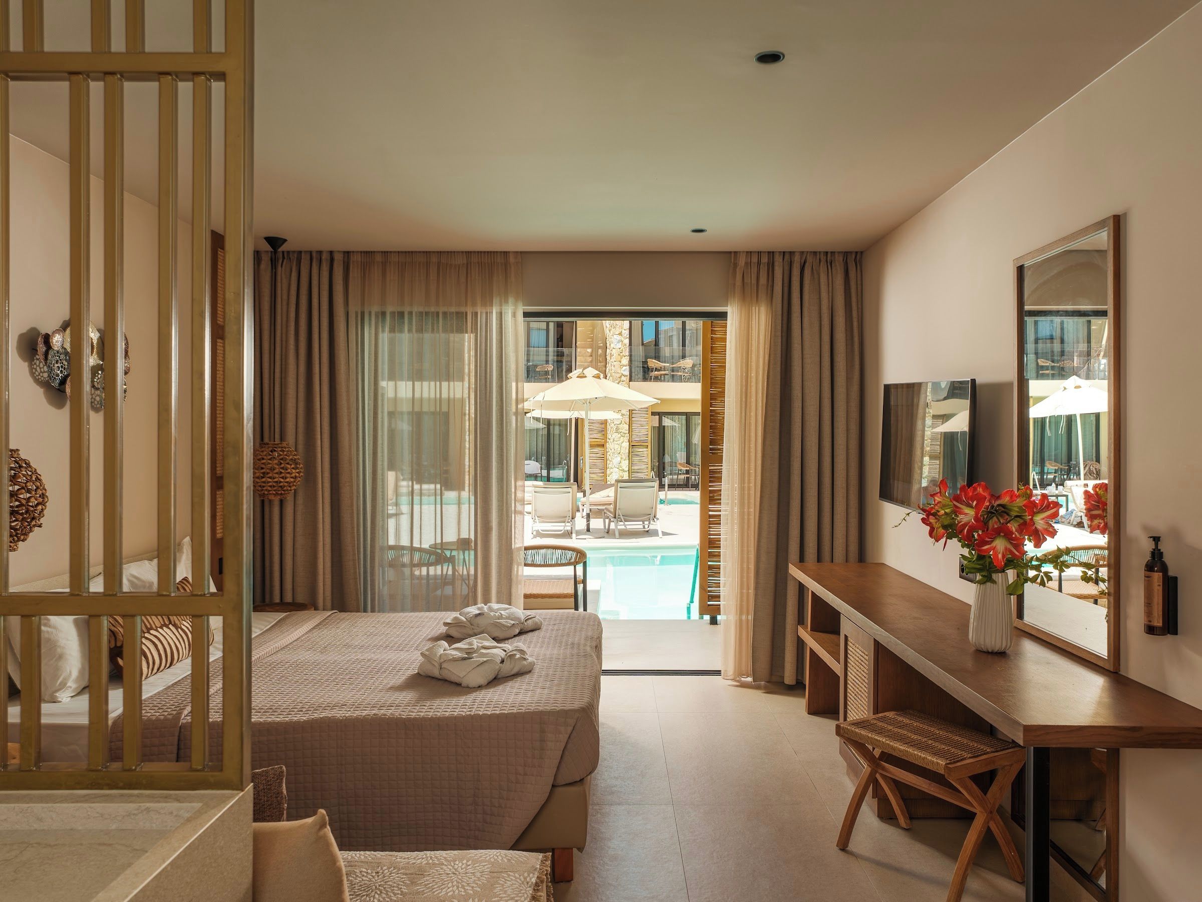 Ein Hotelzimmer mit Bett, Schreibtisch, Sessel, Fernseher und Blick auf einen Außenpool.