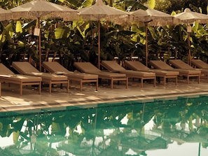 Un área junto a la piscina con sillones reclinables y sombrillas.