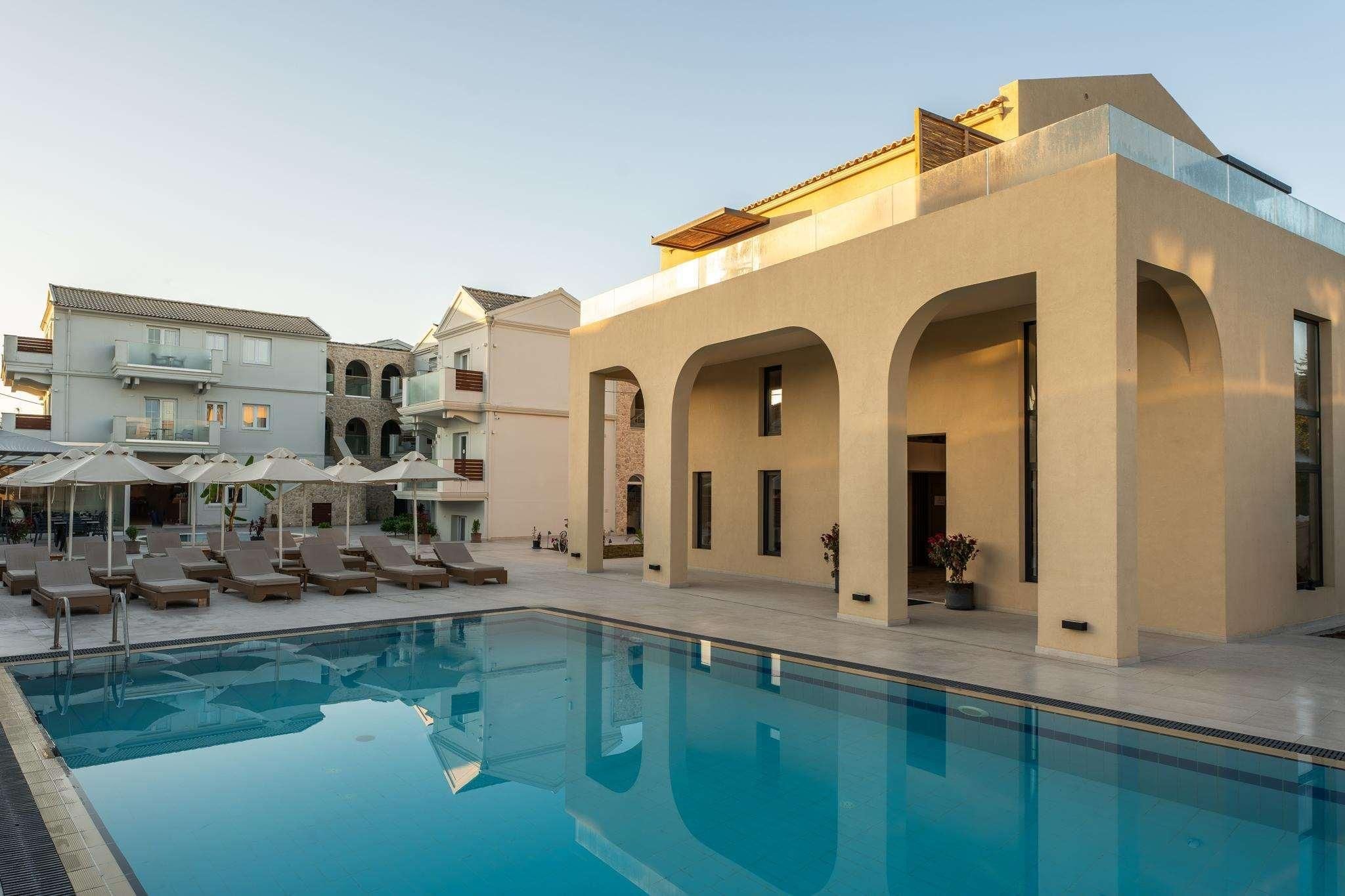 A swimming pool with lounge chairs, a building with arches, and a clear sky.