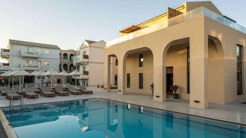A swimming pool with lounge chairs, a building with arches, and a clear sky.