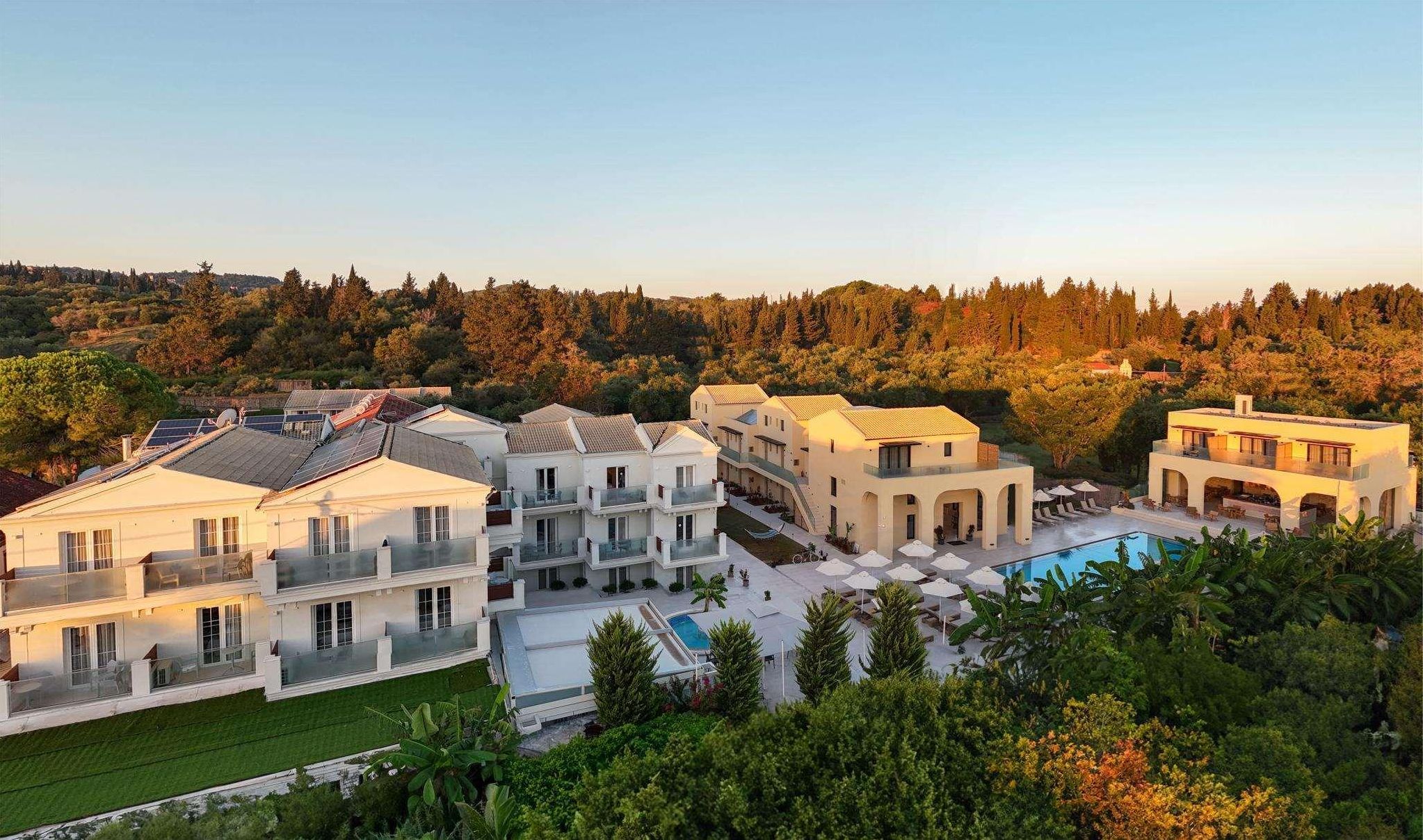 A resort with multiple villas, a swimming pool, and a forested backdrop.