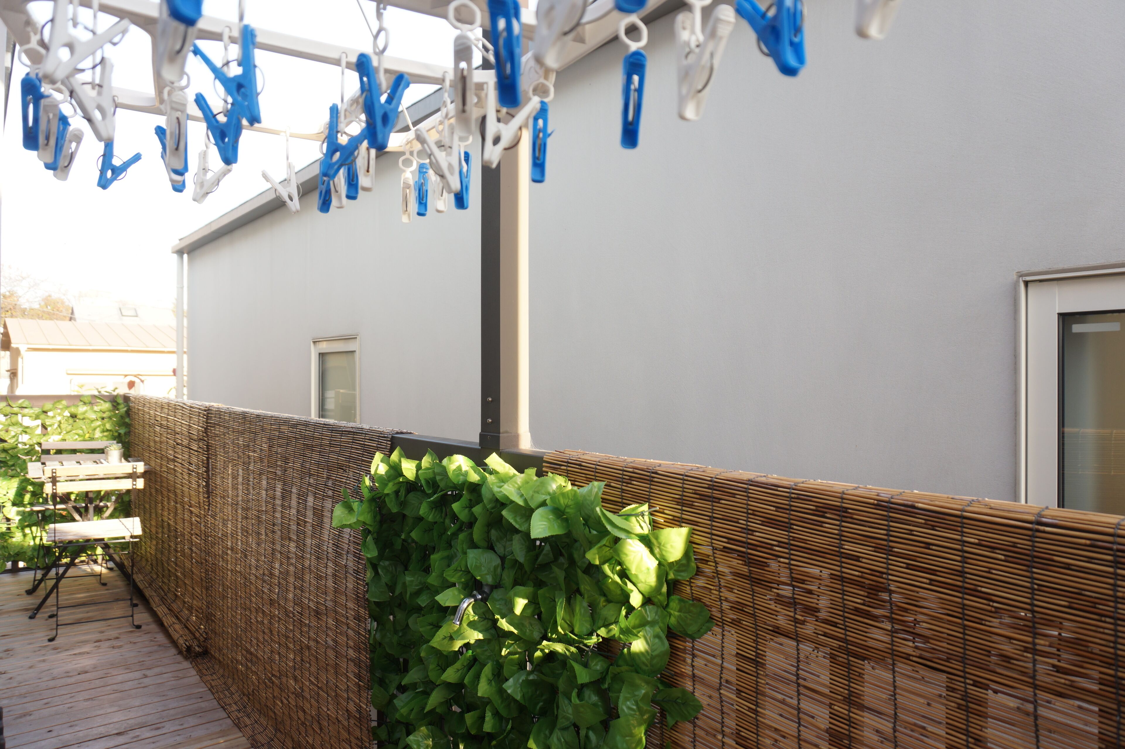 Een balkon met een rieten wand, een metalen hekwerk en een waslijn met blauwe en witte knijpers.