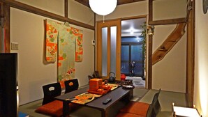 Une pièce de style japonais traditionnel, avec un sol recouvert de tatamis, une petite table basse avec des coussins, une porte coulissante et une vue sur l’extérieur.