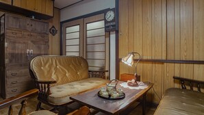 Une pièce de style traditionnel, avec un buffet en bois, un canapé confortable, une table en bois sur laquelle est posée une théière, et une horloge au mur.