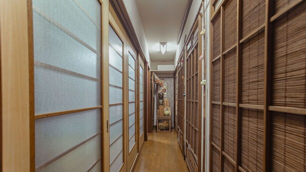 Un couloir étroit, avec des portes coulissantes traditionnelles de chaque côté, un plancher en bois et une petite table placée au centre, sur laquelle se trouvent divers objets.