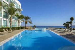 Ein Pool mit Liegestühlen und Palmen, mit Blick auf den Ozean.