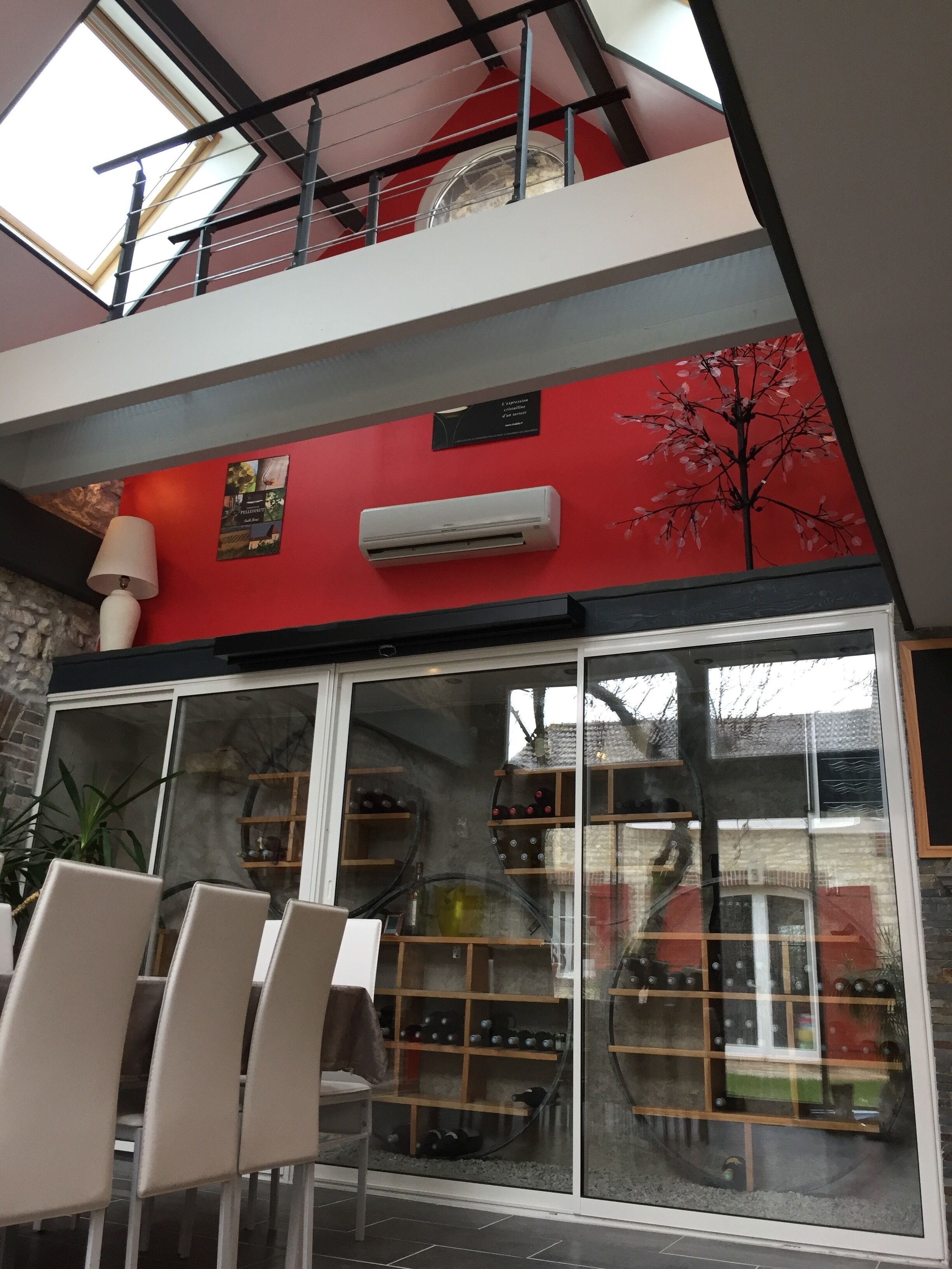 A modern interior with a red accent wall, a skylight, and a wine rack visible through a glass door.