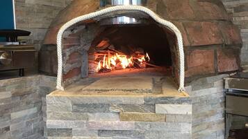 A brick oven pizza oven with a chimney, stone walls, and a fire burning inside.