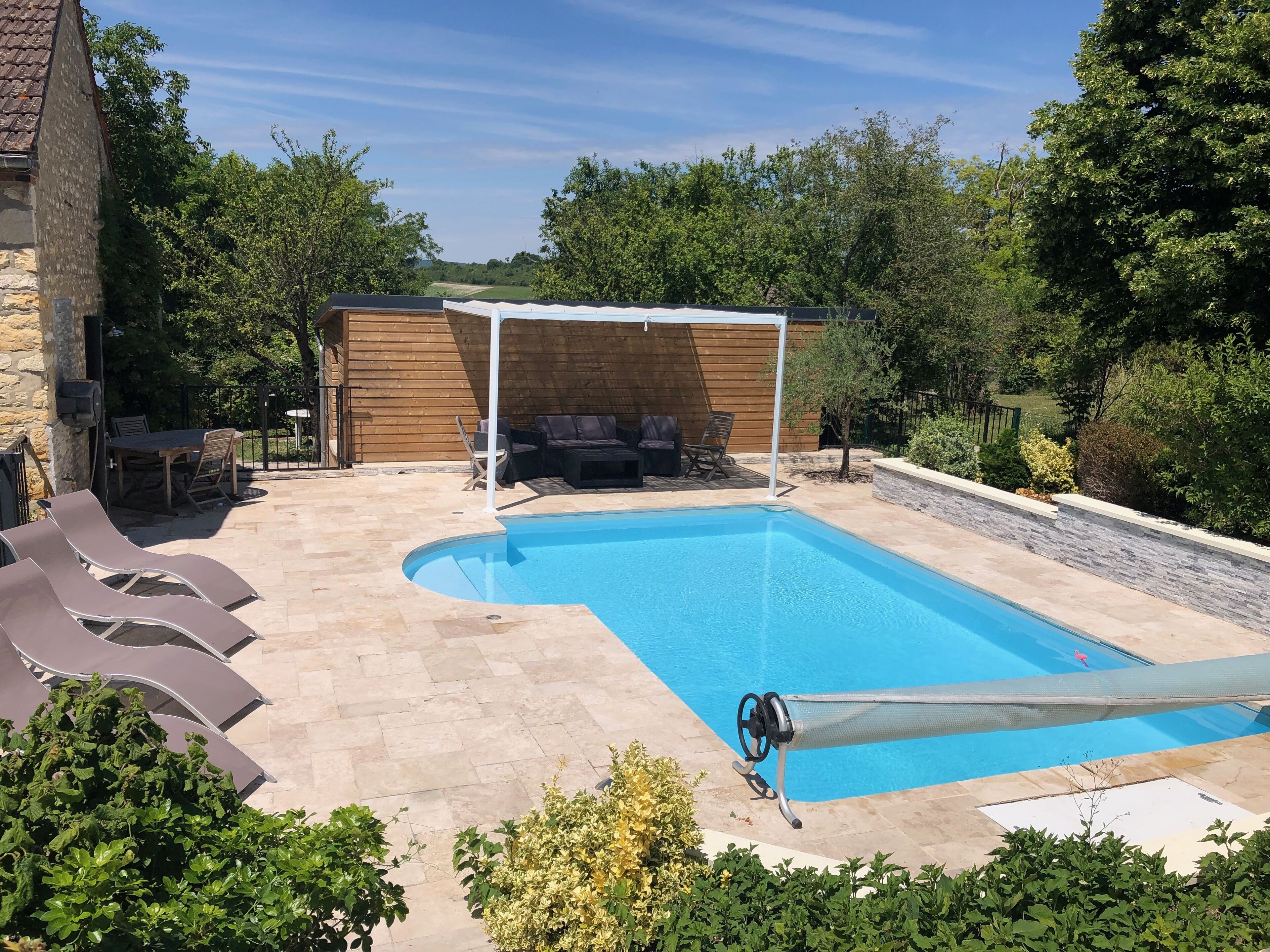 A swimming pool with a sunshade, lounge chairs, and a wooden deck.