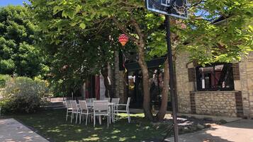 Een terras met tafels en stoelen, een basketbalring en een stenen gebouw met een raam.