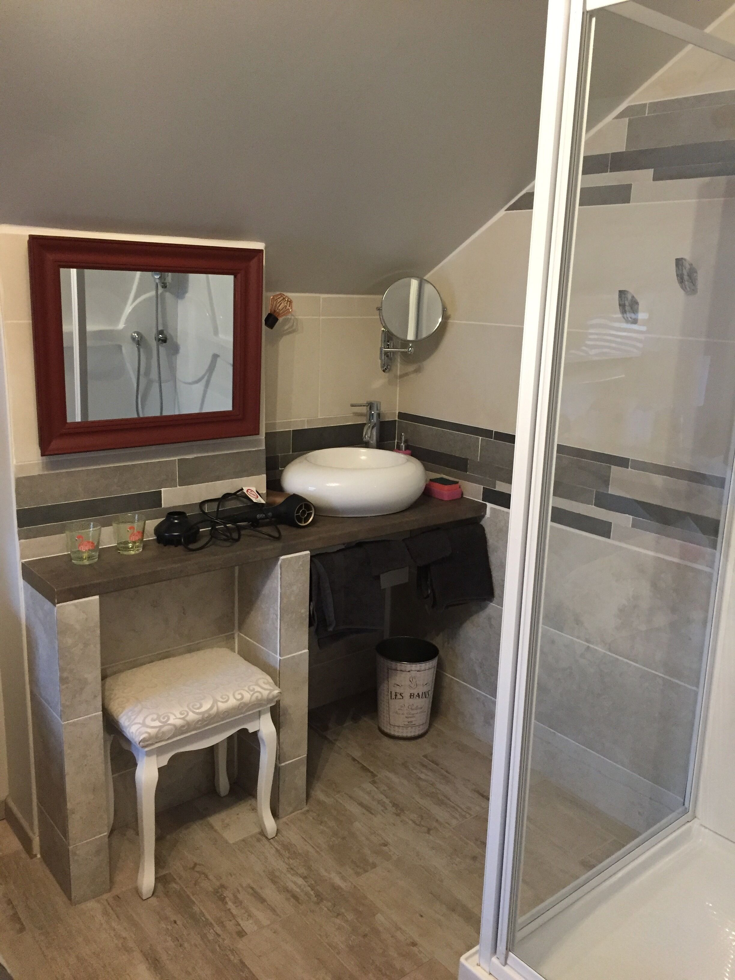 A bathroom with a white sink, a mirror above it, a shower area, and a bench.