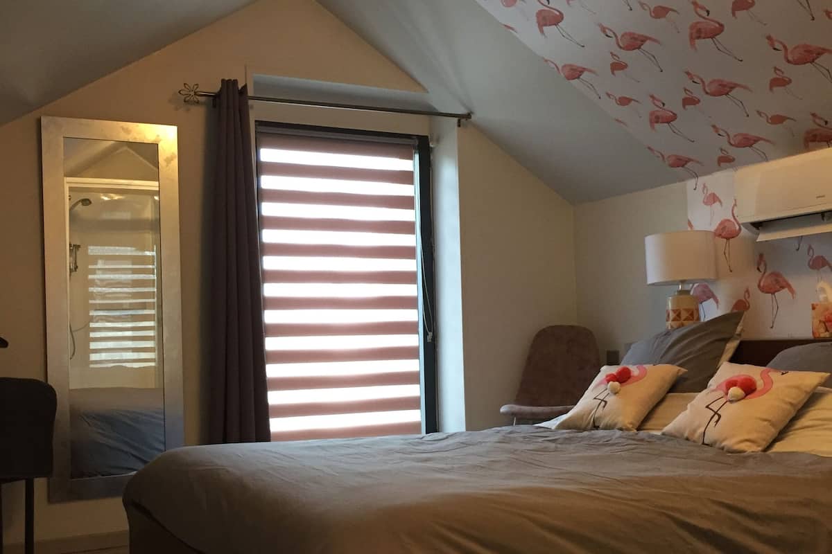 A bedroom with a bed, a chair, a desk, and a window with blinds.