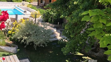 Um quintal com piscina, um deck de madeira e um pequeno edifício com telhado vermelho.