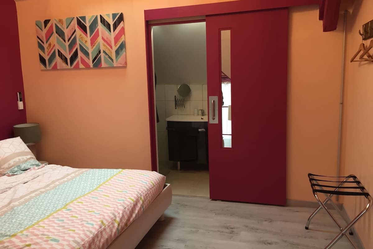 A bedroom with a bed, a door leading to a bathroom, and a mirror on the wall.
