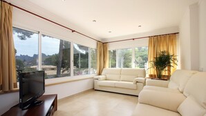 A spacious living room with a large window, a sofa, a TV on a wooden stand, and a potted plant. - MEDINA. Modern villa just 325 m from crystal clear beaches (Cala San Vicente)